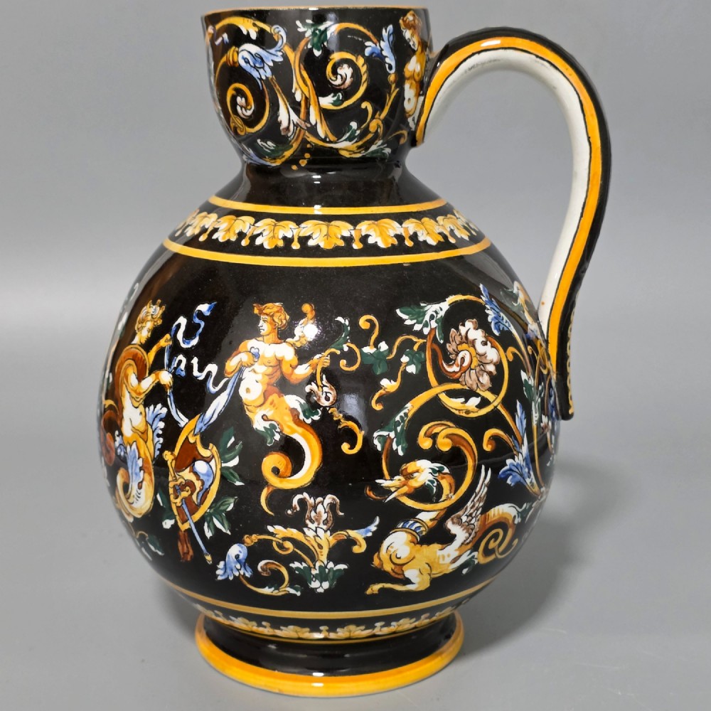 A nineteenth-century French Gien faience water pitcher featuring a black glazed body decorated with hand-painted ochre, white, and blue Renaissance revival mythological figures and scrolling foliage.