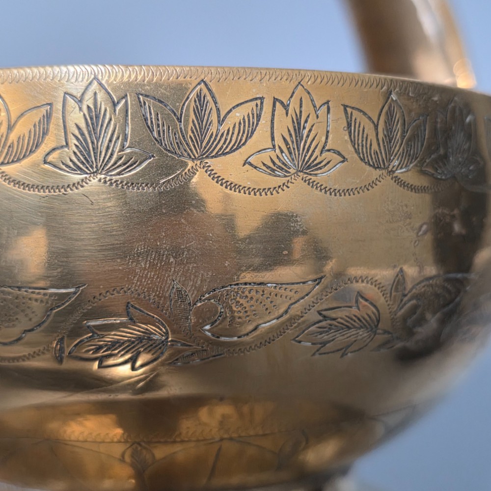 An antique Indian engraved brass kamandal vessel featuring a rounded base decorated with figures, a flared upper rim, and a high arched handle with raised knops. View IV