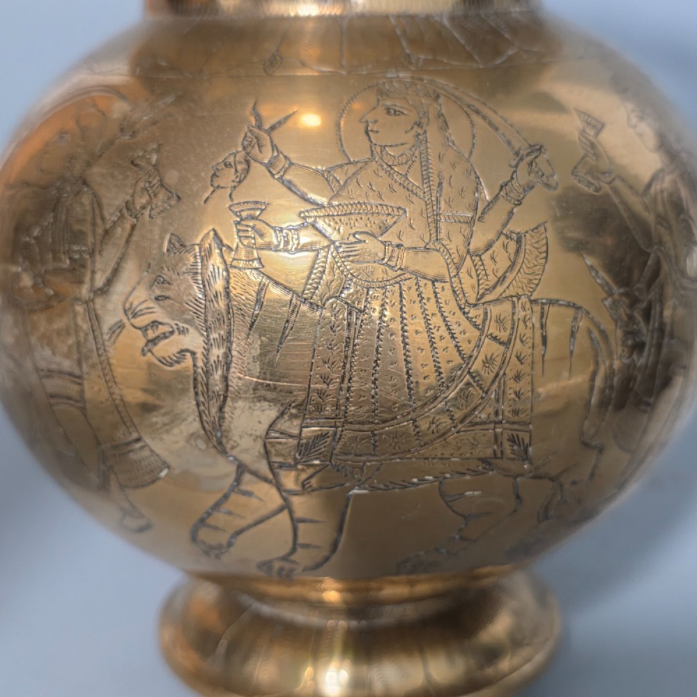 An antique Indian engraved brass kamandal vessel featuring a rounded base decorated with figures, a flared upper rim, and a high arched handle with raised knops. View V