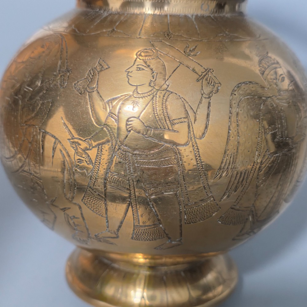 An antique Indian engraved brass kamandal vessel featuring a rounded base decorated with figures, a flared upper rim, and a high arched handle with raised knops. View VI