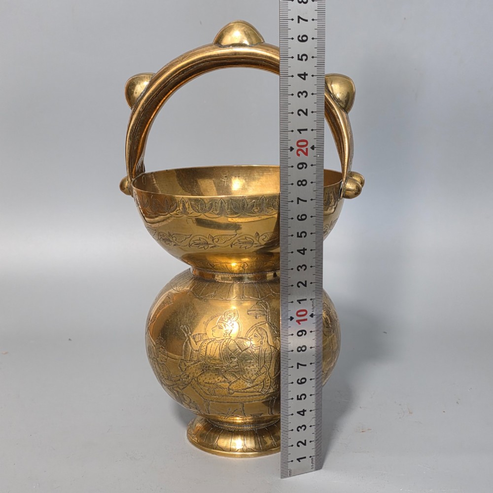 An antique Indian engraved brass kamandal vessel featuring a rounded base decorated with figures, a flared upper rim, and a high arched handle with raised knops. View IX