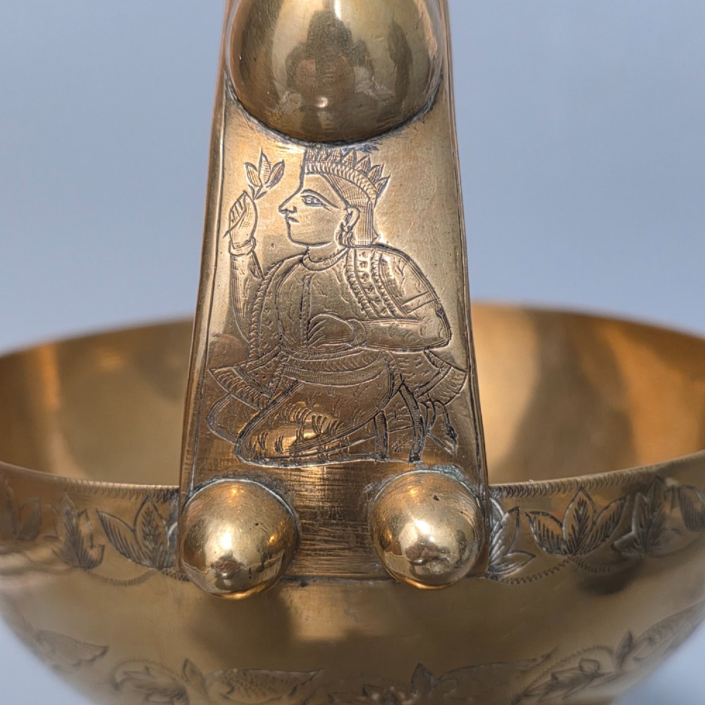 An antique Indian engraved brass kamandal vessel featuring a rounded base decorated with figures, a flared upper rim, and a high arched handle with raised knops. View XII
