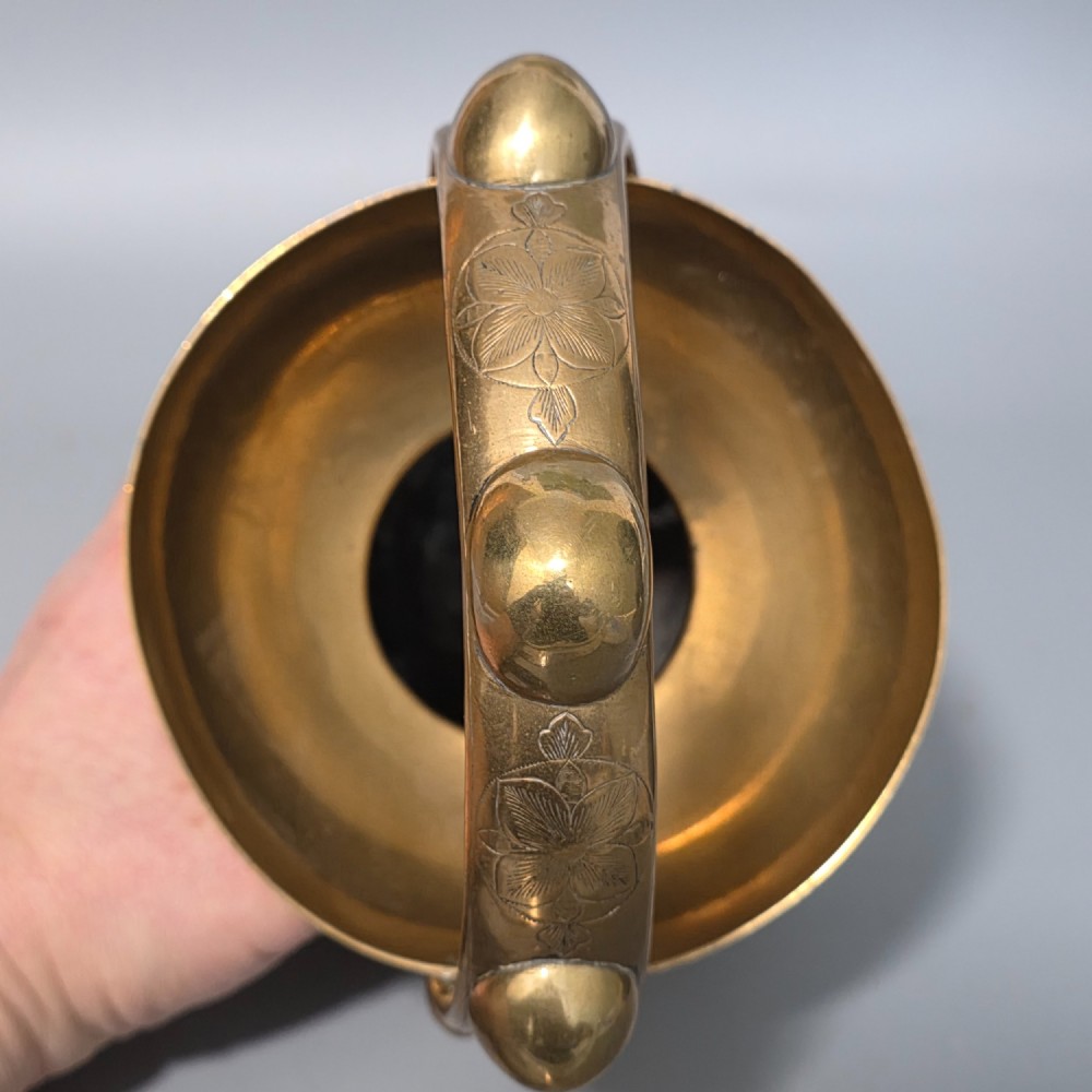 An antique Indian engraved brass kamandal vessel featuring a rounded base decorated with figures, a flared upper rim, and a high arched handle with raised knops. View XV