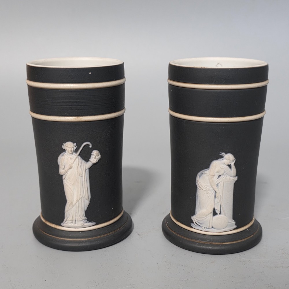 A pair of cylindrical black basalt spill holders featuring raised white neoclassical figures and white double-banded rims.