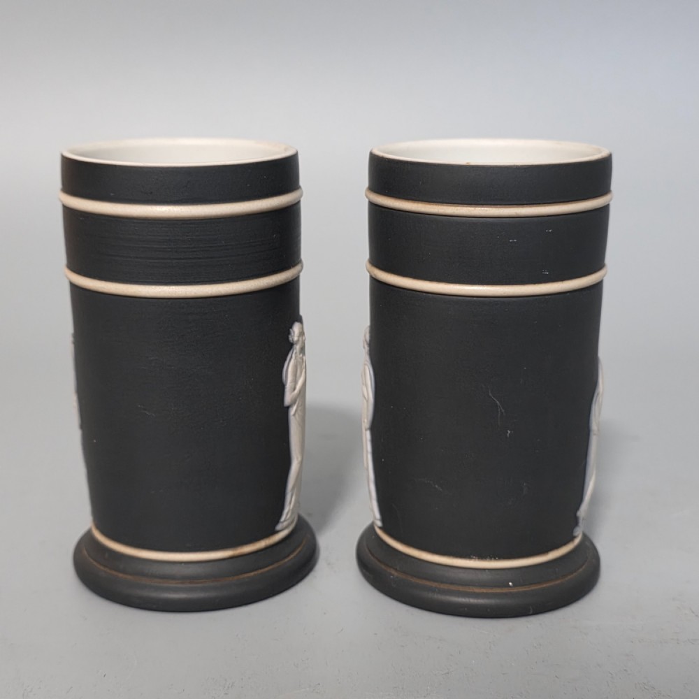 A pair of cylindrical black basalt spill holders featuring raised white neoclassical figures and white double-banded rims. View IV