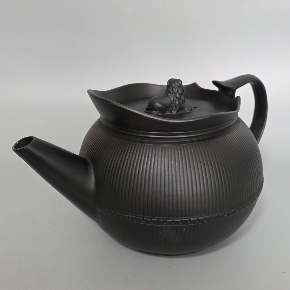 An 18th-century matte black basalt teapot featuring vertical engine-turned fluting, a curved spout, and a lid crowned with a sculpted lion finial. View II