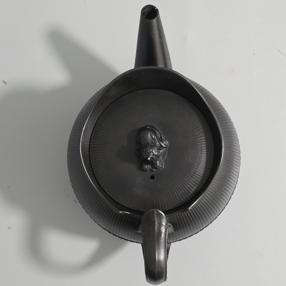 An 18th-century matte black basalt teapot featuring vertical engine-turned fluting, a curved spout, and a lid crowned with a sculpted lion finial. View XII