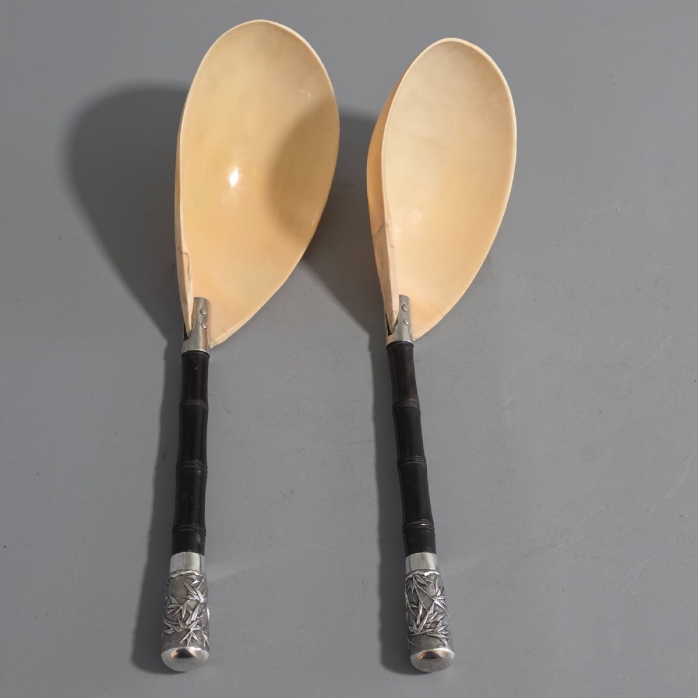 A pair of Chinese export silver salad servers featuring carved shell bowls, dark wooden bamboo-form handles, and silver terminal caps chased with bamboo leaves.