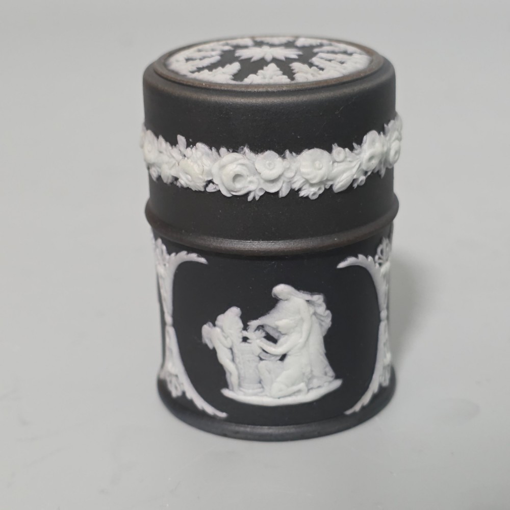 A cylindrical black stoneware Wedgwood match striker featuring white classical relief figures and floral garlands.