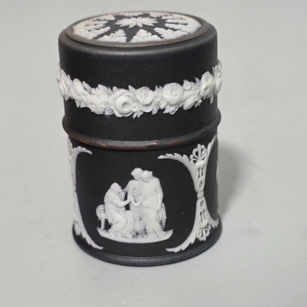 A cylindrical black stoneware Wedgwood match striker featuring white classical relief figures and floral garlands. View II