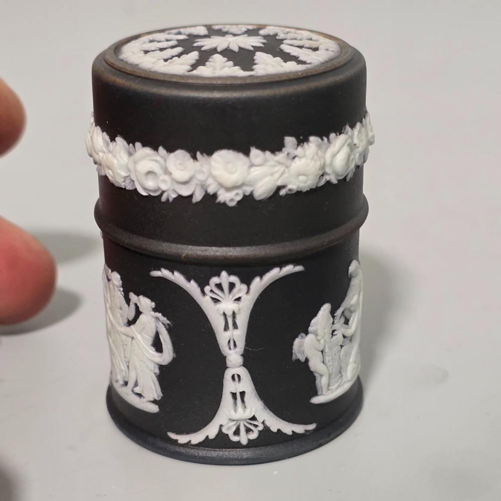 A cylindrical black stoneware Wedgwood match striker featuring white classical relief figures and floral garlands. View IV