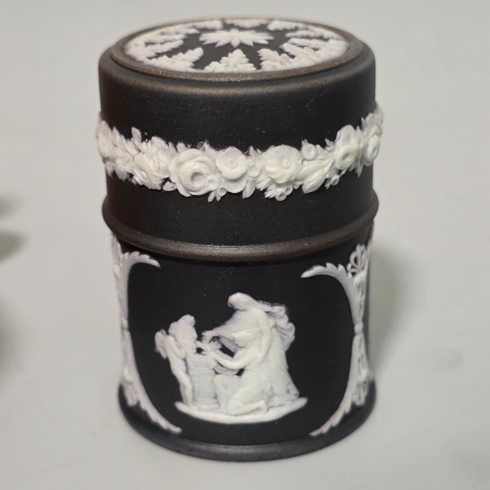 A cylindrical black stoneware Wedgwood match striker featuring white classical relief figures and floral garlands. View V