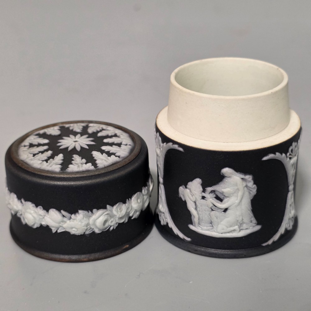 A cylindrical black stoneware Wedgwood match striker featuring white classical relief figures and floral garlands. View VII