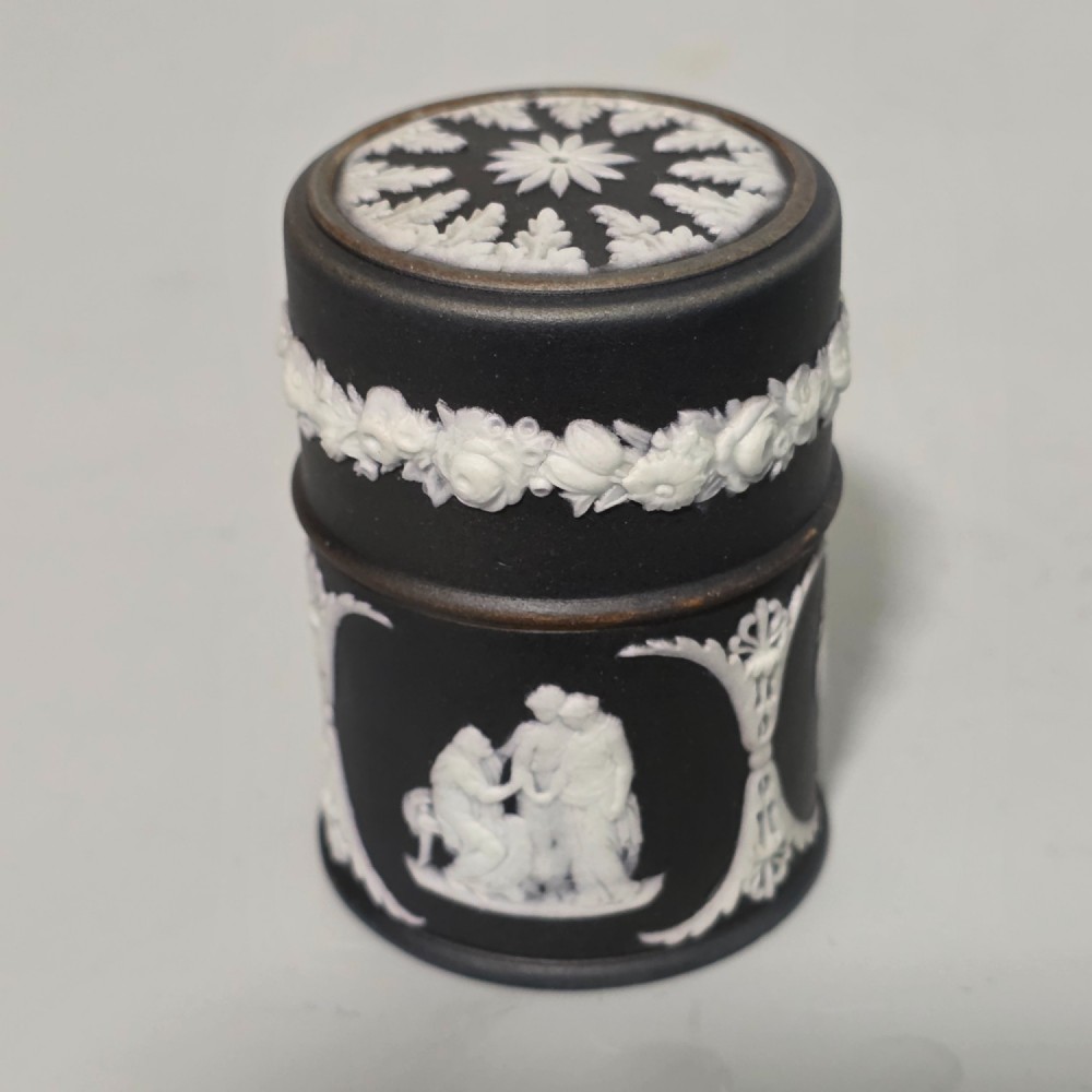 A cylindrical black stoneware Wedgwood match striker featuring white classical relief figures and floral garlands. View X