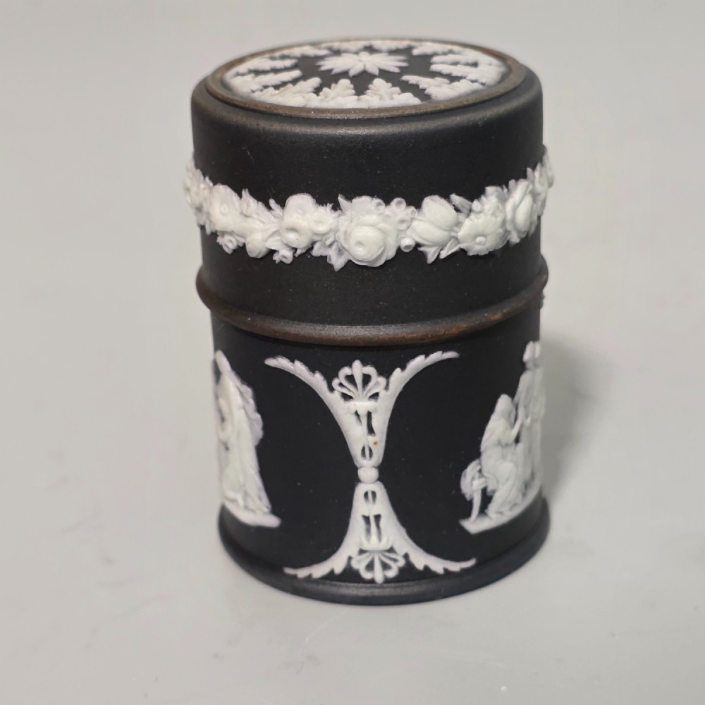 A cylindrical black stoneware Wedgwood match striker featuring white classical relief figures and floral garlands. View XI