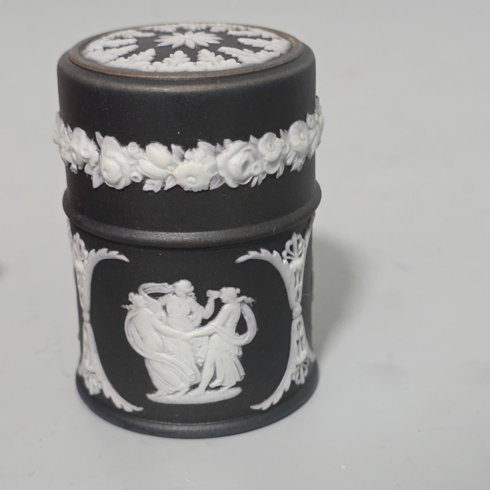 A cylindrical black stoneware Wedgwood match striker featuring white classical relief figures and floral garlands. View XII