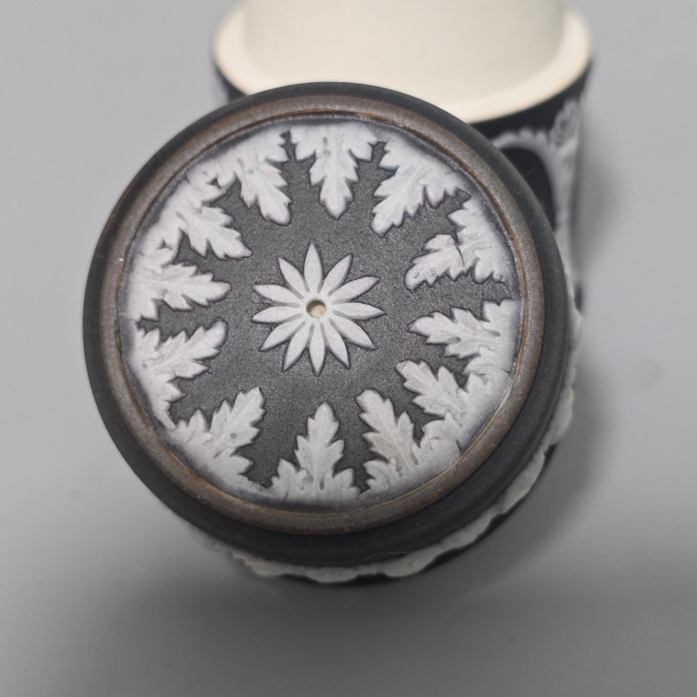 A cylindrical black stoneware Wedgwood match striker featuring white classical relief figures and floral garlands. View XIII