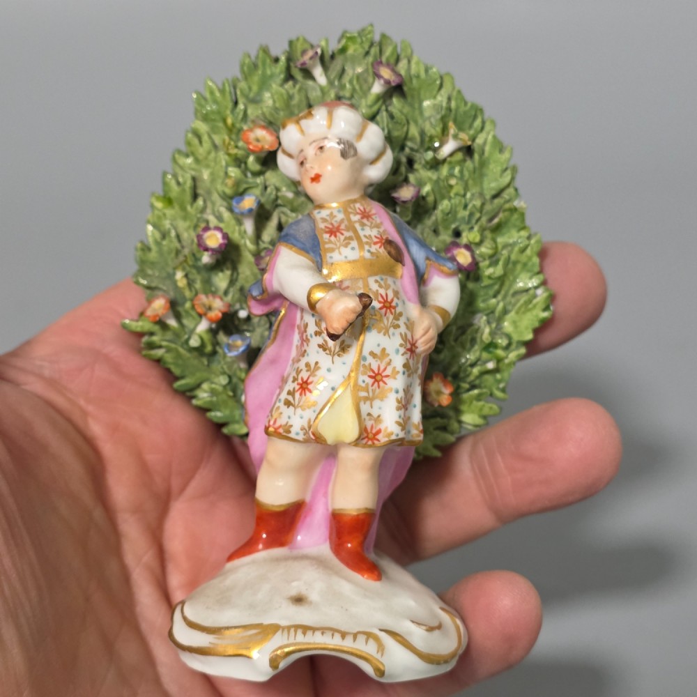 A pair of 19th-century hand-painted porcelain figurines featuring male and female characters in detailed costume before dense floral bocage backdrops on gilded scroll bases. View VI