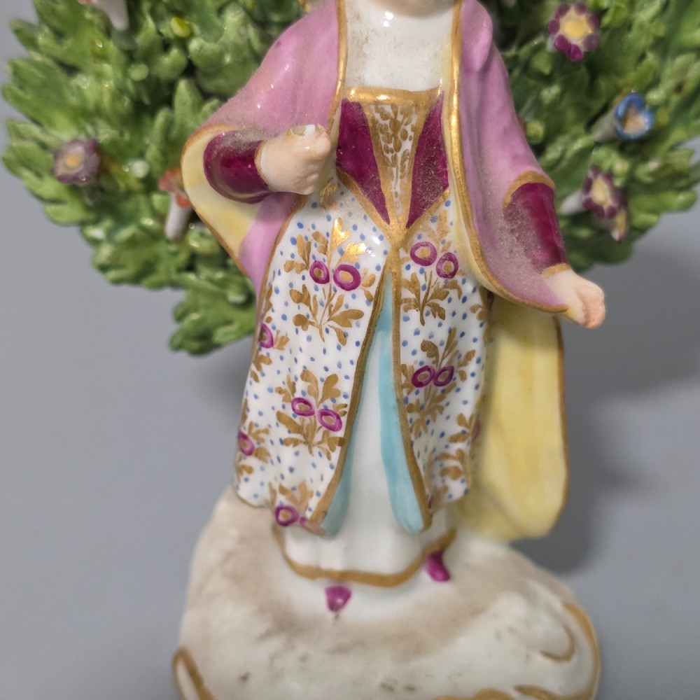 A pair of 19th-century hand-painted porcelain figurines featuring male and female characters in detailed costume before dense floral bocage backdrops on gilded scroll bases. View VII