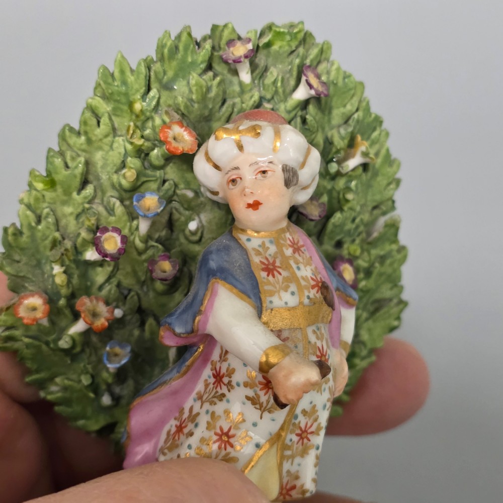 A pair of 19th-century hand-painted porcelain figurines featuring male and female characters in detailed costume before dense floral bocage backdrops on gilded scroll bases. View VIII