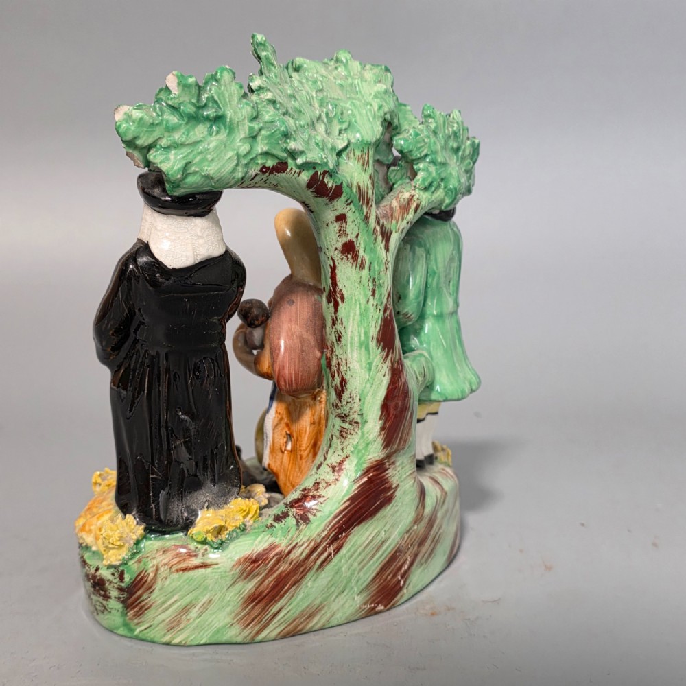 An early 19th-century Staffordshire ceramic figure group depicting a farmer, his wife holding a baby, and a parson standing before a flowering bocage tree. View III