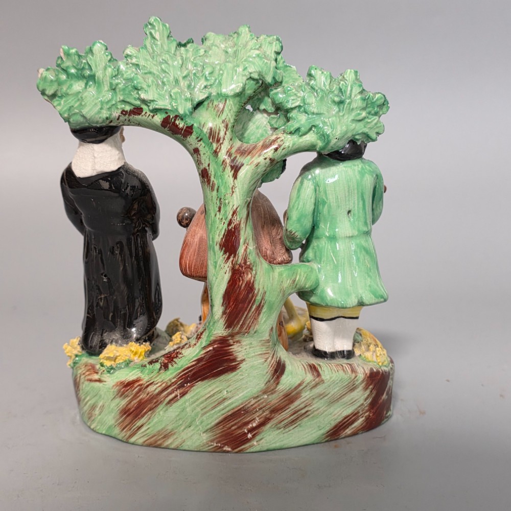 An early 19th-century Staffordshire ceramic figure group depicting a farmer, his wife holding a baby, and a parson standing before a flowering bocage tree. View IV