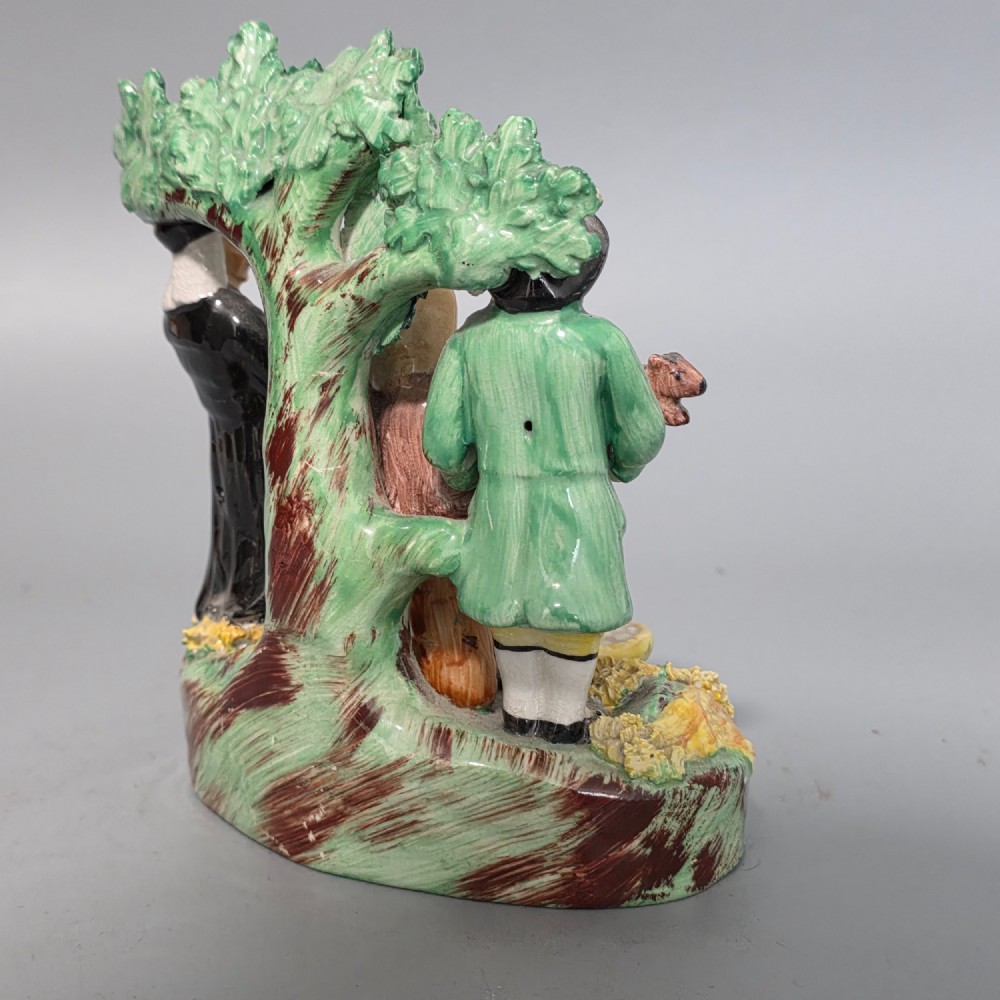 An early 19th-century Staffordshire ceramic figure group depicting a farmer, his wife holding a baby, and a parson standing before a flowering bocage tree. View V