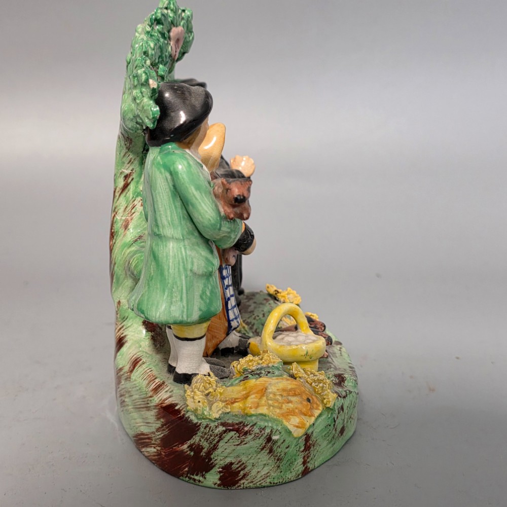 An early 19th-century Staffordshire ceramic figure group depicting a farmer, his wife holding a baby, and a parson standing before a flowering bocage tree. View VI