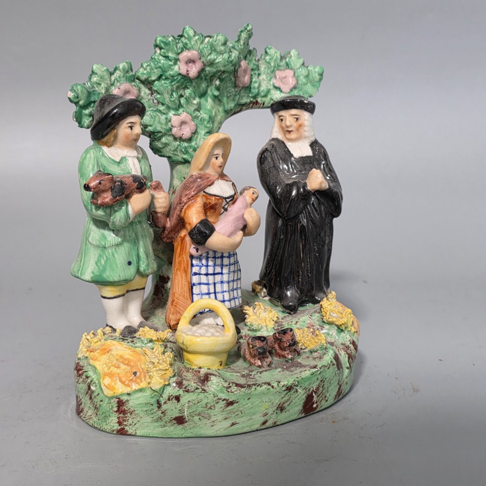 An early 19th-century Staffordshire ceramic figure group depicting a farmer, his wife holding a baby, and a parson standing before a flowering bocage tree. View VII