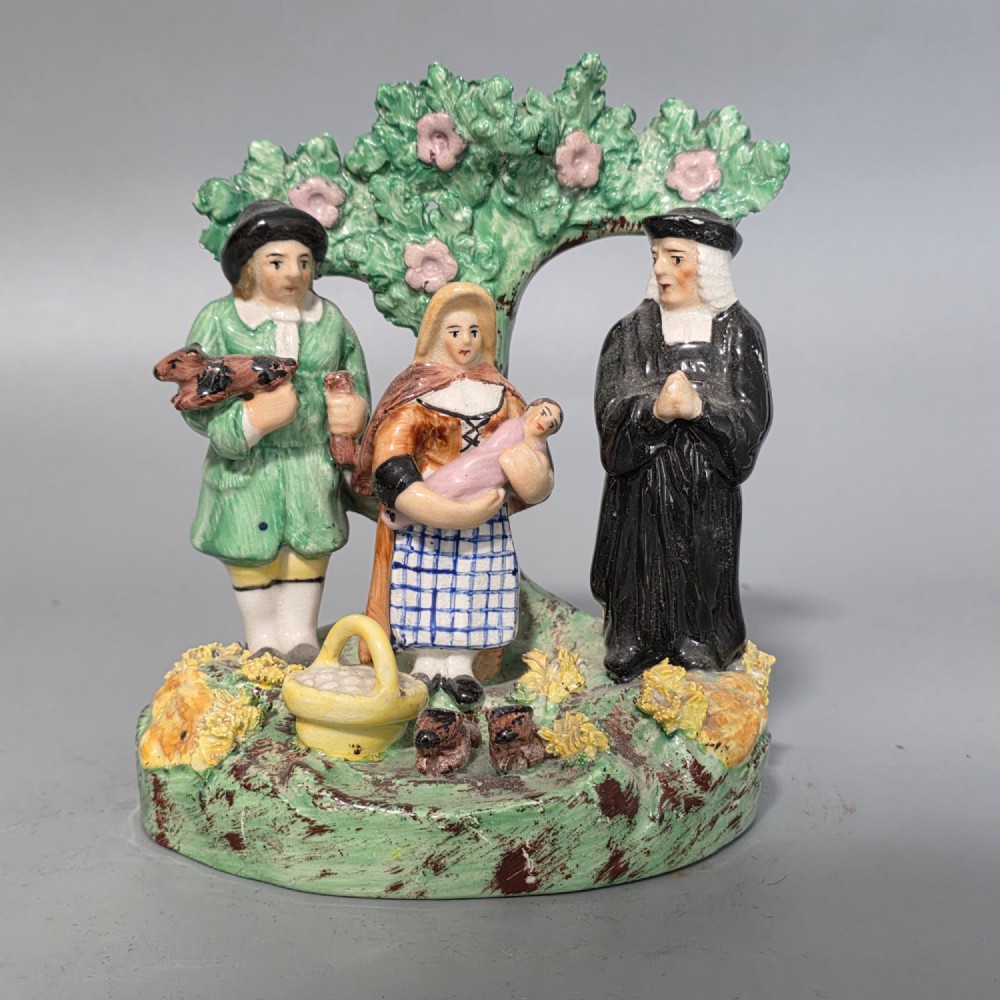 An early 19th-century Staffordshire ceramic figure group depicting a farmer, his wife holding a baby, and a parson standing before a flowering bocage tree. View VIII