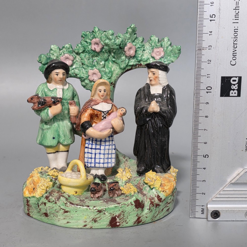 An early 19th-century Staffordshire ceramic figure group depicting a farmer, his wife holding a baby, and a parson standing before a flowering bocage tree. View II
