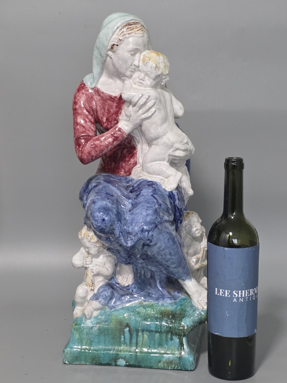 A polychrome glazed ceramic sculpture depicting an enthroned Madonna holding the Christ Child with a small musical putto playing at her feet. View II