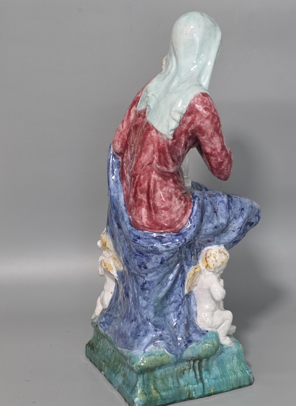 A polychrome glazed ceramic sculpture depicting an enthroned Madonna holding the Christ Child with a small musical putto playing at her feet. View V