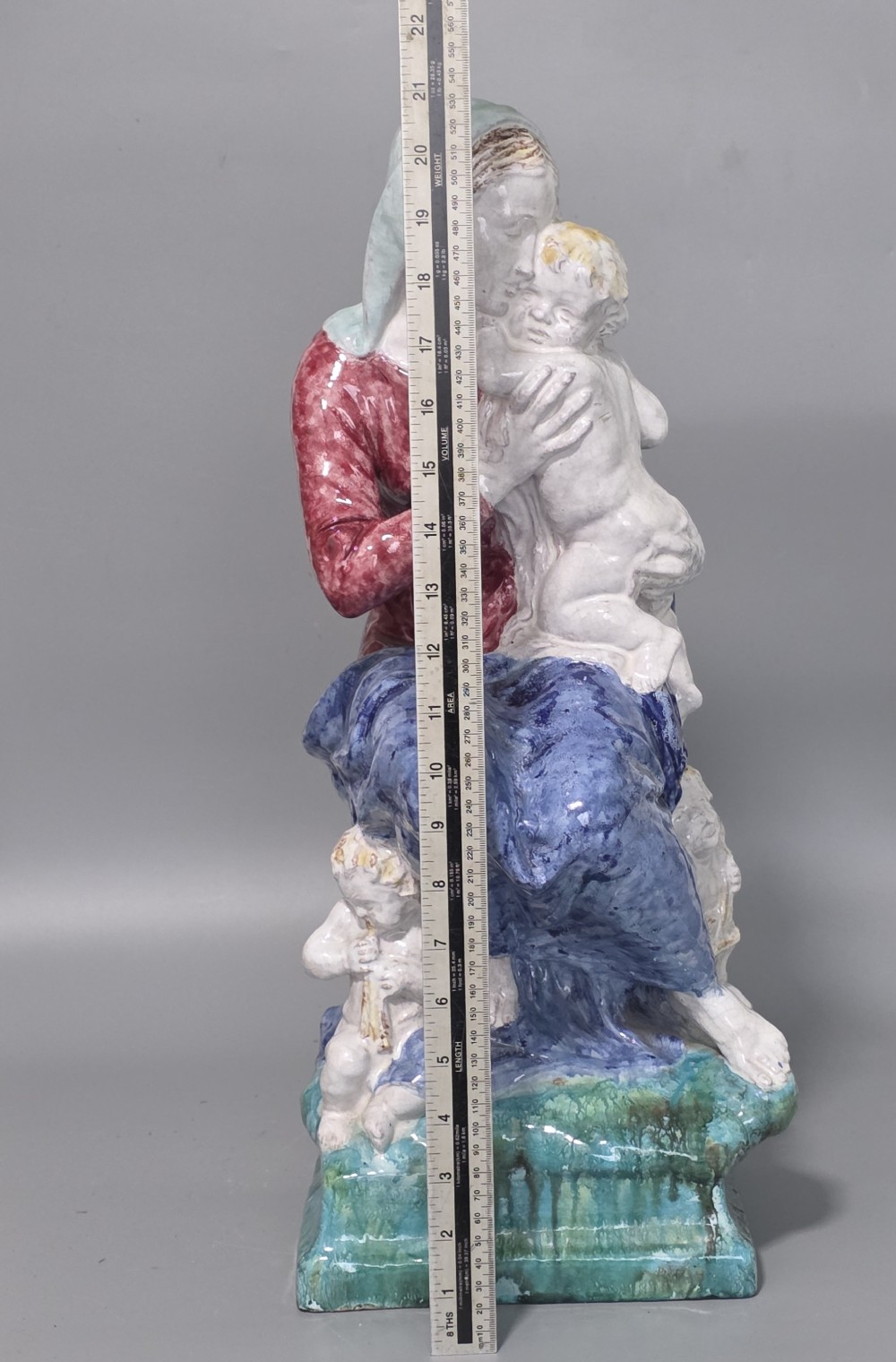 A polychrome glazed ceramic sculpture depicting an enthroned Madonna holding the Christ Child with a small musical putto playing at her feet. View VII