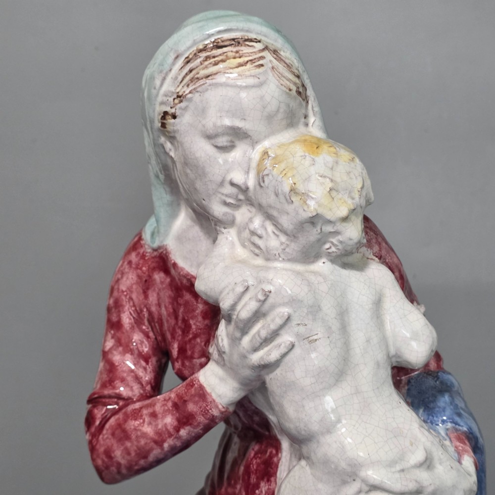 A polychrome glazed ceramic sculpture depicting an enthroned Madonna holding the Christ Child with a small musical putto playing at her feet. View X