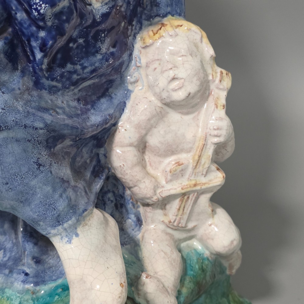 A polychrome glazed ceramic sculpture depicting an enthroned Madonna holding the Christ Child with a small musical putto playing at her feet. View XI