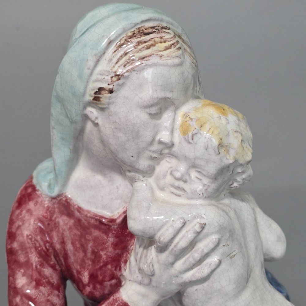 A polychrome glazed ceramic sculpture depicting an enthroned Madonna holding the Christ Child with a small musical putto playing at her feet. View XII