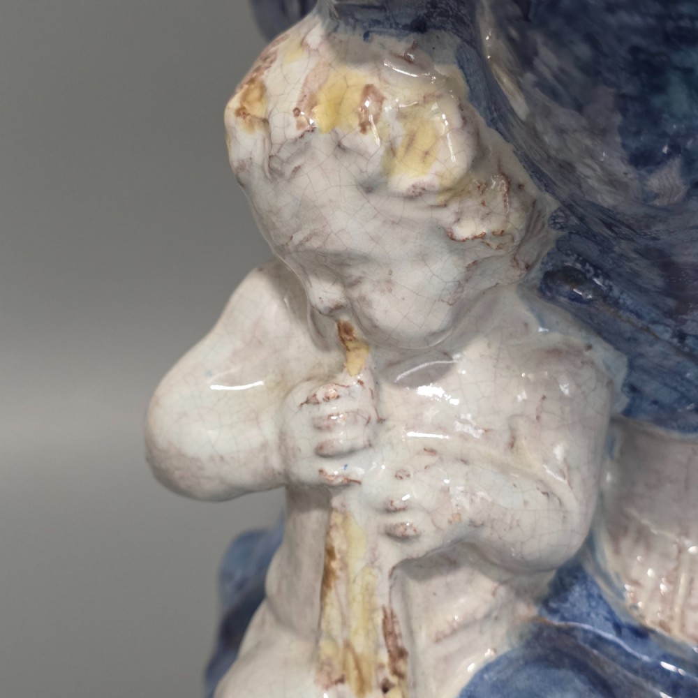 A polychrome glazed ceramic sculpture depicting an enthroned Madonna holding the Christ Child with a small musical putto playing at her feet. View XIII