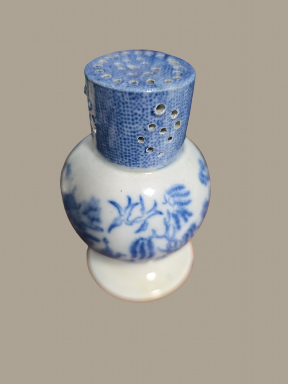 An antique blue and white pearlware pepper pot featuring transfer-printed chinoiserie motifs and a perforated cylindrical top.
