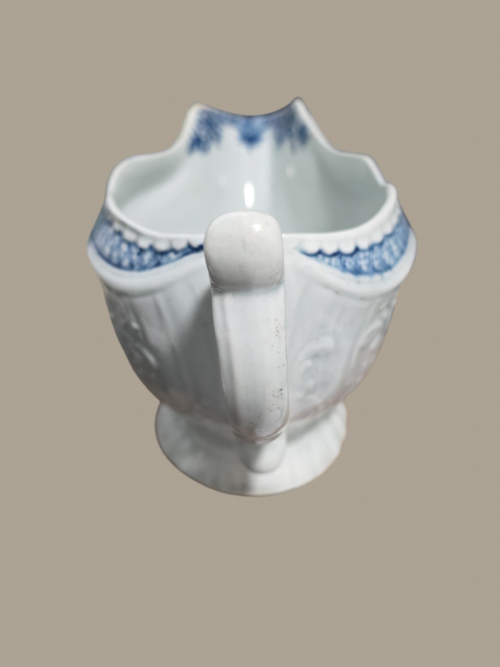 An eighteenth-century blue and white soft-paste porcelain sauce boat featuring moulded scroll decoration, a shaped rim, a scroll handle, and a printed landscape scene. View II
