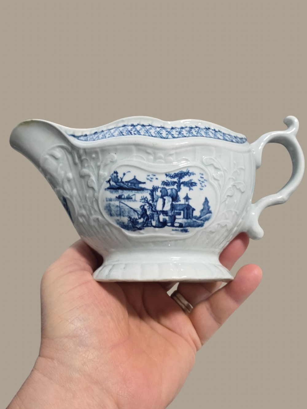 An eighteenth-century blue and white soft-paste porcelain sauce boat featuring moulded scroll decoration, a shaped rim, a scroll handle, and a printed landscape scene. View III