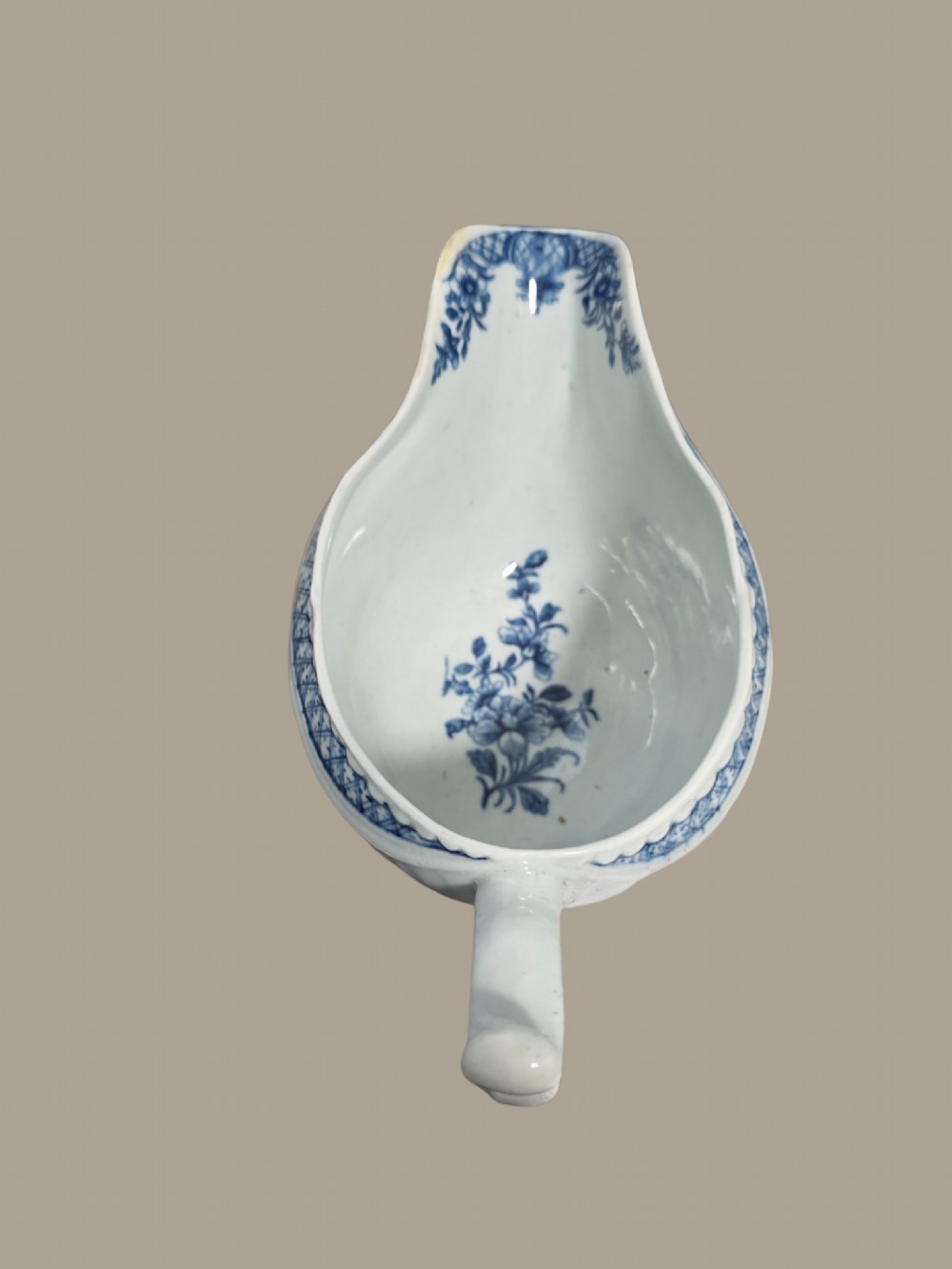 An eighteenth-century blue and white soft-paste porcelain sauce boat featuring moulded scroll decoration, a shaped rim, a scroll handle, and a printed landscape scene. View IV