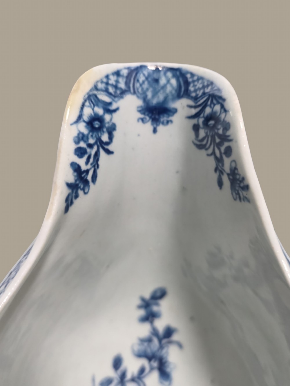 An eighteenth-century blue and white soft-paste porcelain sauce boat featuring moulded scroll decoration, a shaped rim, a scroll handle, and a printed landscape scene. View VII