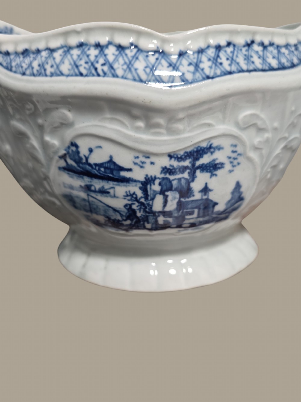 An eighteenth-century blue and white soft-paste porcelain sauce boat featuring moulded scroll decoration, a shaped rim, a scroll handle, and a printed landscape scene. View VIII