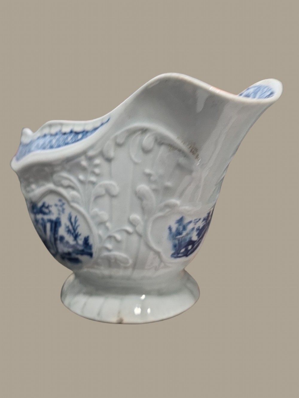 An eighteenth-century blue and white soft-paste porcelain sauce boat featuring moulded scroll decoration, a shaped rim, a scroll handle, and a printed landscape scene. View XIII