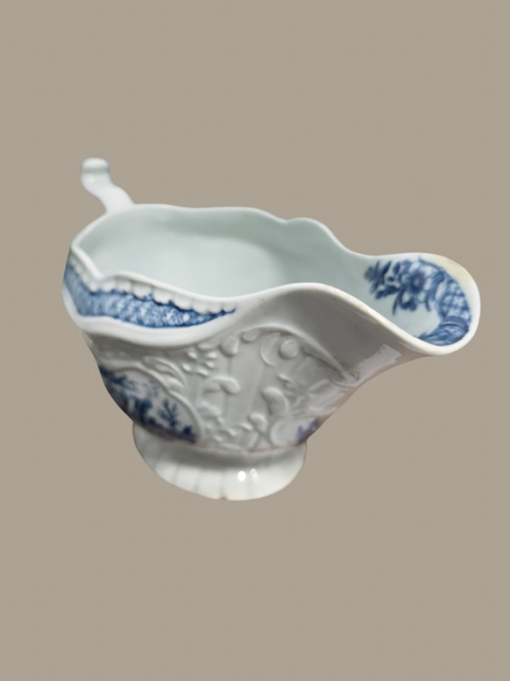 An eighteenth-century blue and white soft-paste porcelain sauce boat featuring moulded scroll decoration, a shaped rim, a scroll handle, and a printed landscape scene. View XIV