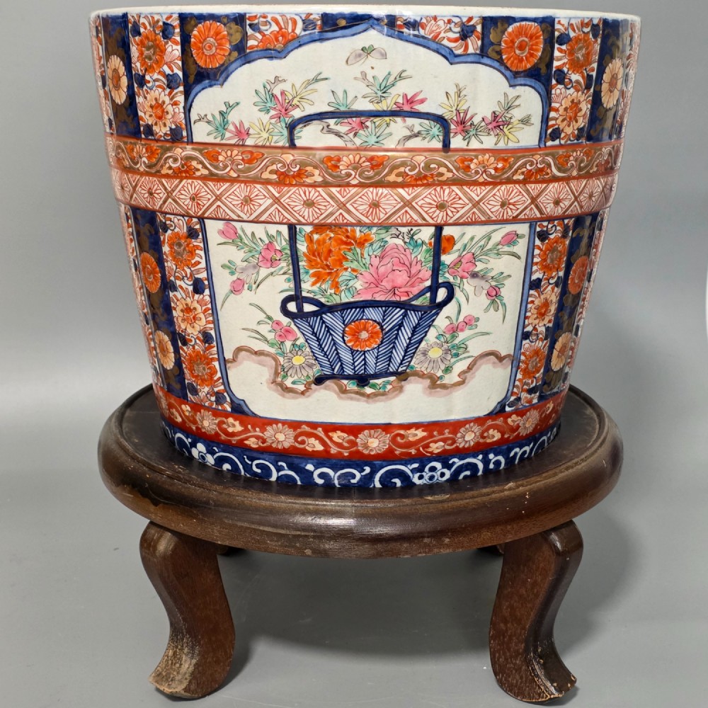 A late 19th-century Japanese Imari porcelain planter decorated with cobalt blue and iron-red floral basket panels, resting on a carved dark wood stand.