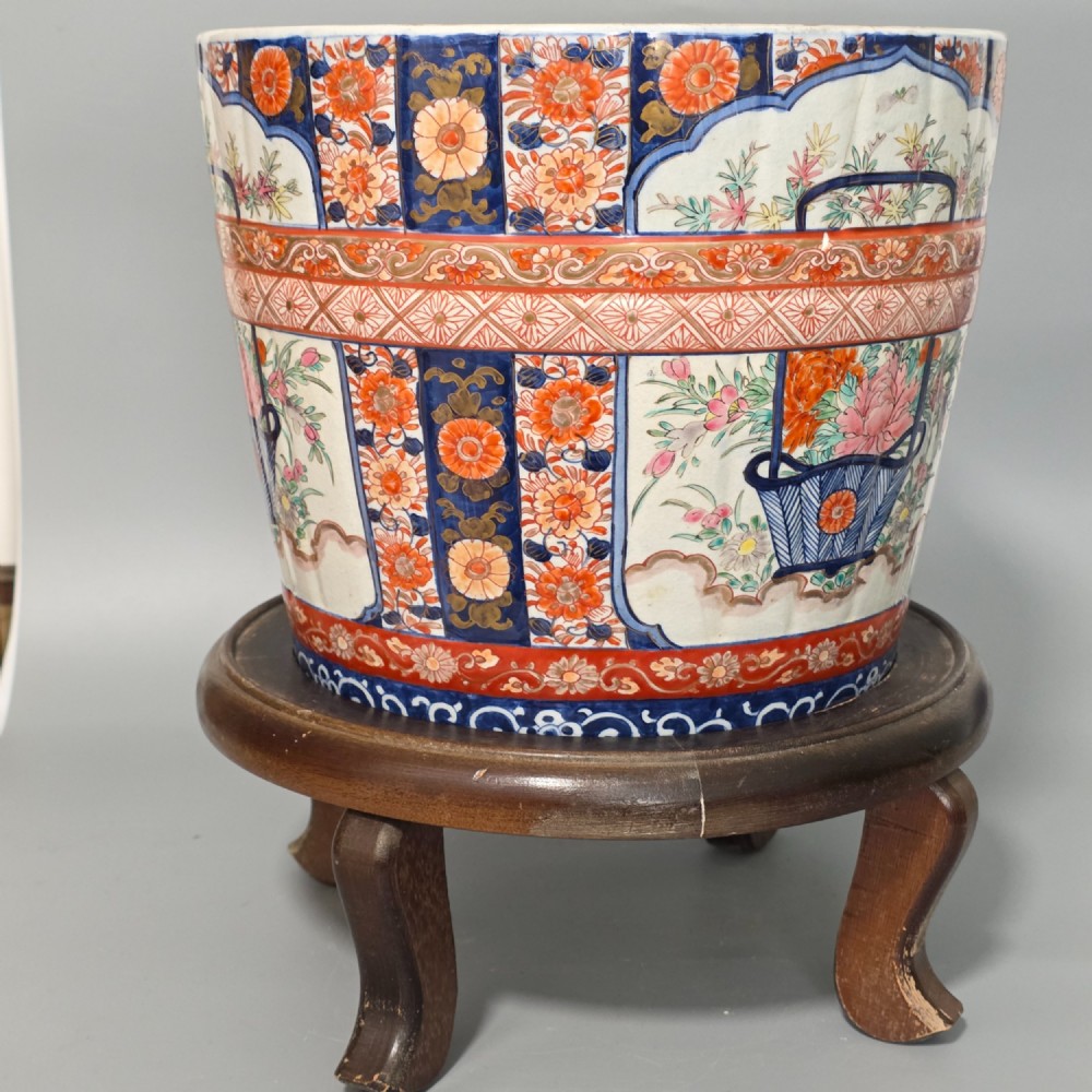 A late 19th-century Japanese Imari porcelain planter decorated with cobalt blue and iron-red floral basket panels, resting on a carved dark wood stand. View II