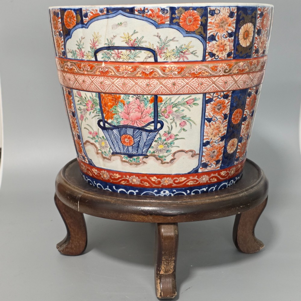 A late 19th-century Japanese Imari porcelain planter decorated with cobalt blue and iron-red floral basket panels, resting on a carved dark wood stand. View III