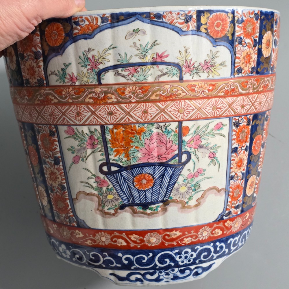 A late 19th-century Japanese Imari porcelain planter decorated with cobalt blue and iron-red floral basket panels, resting on a carved dark wood stand. View IV